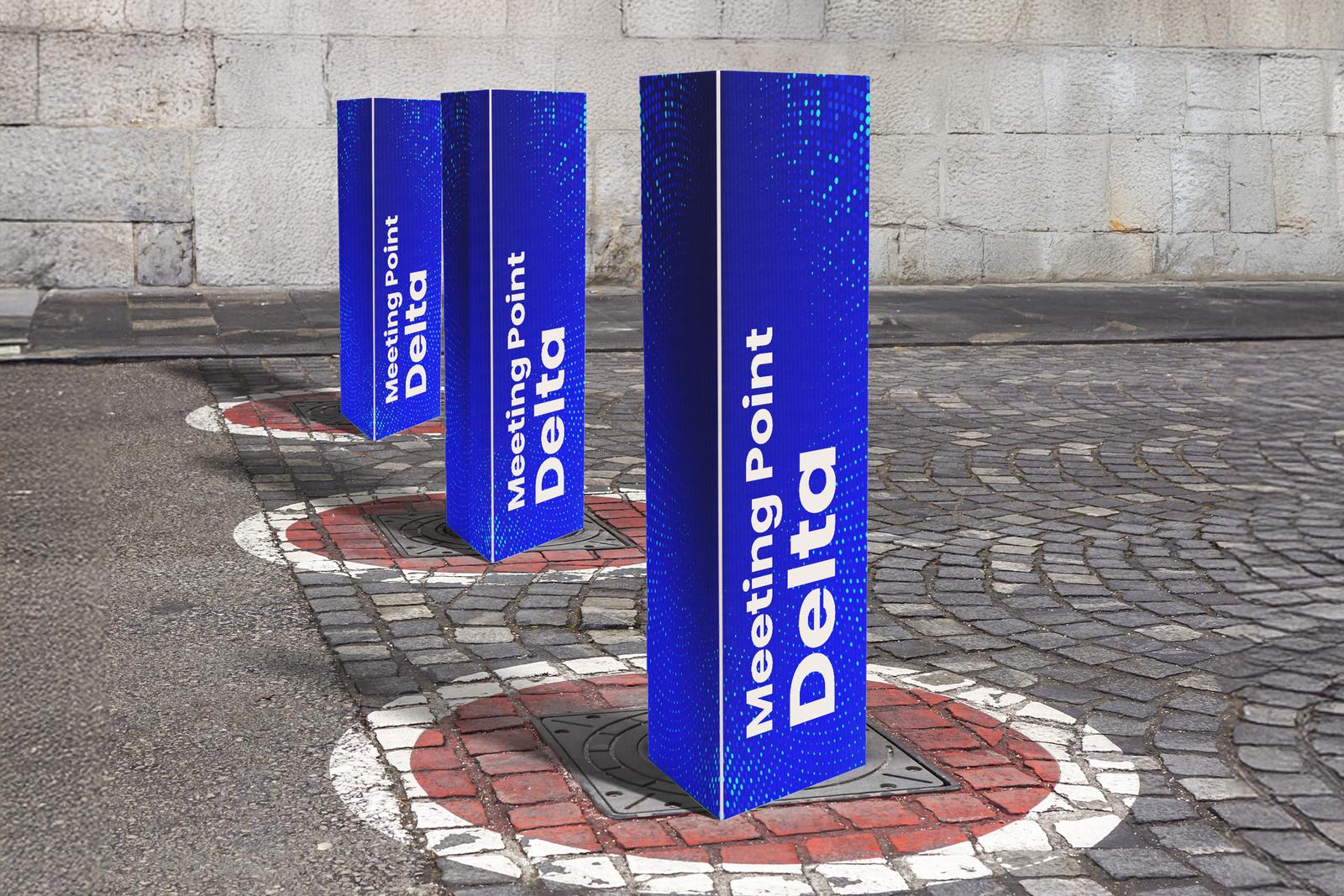 Three blue “Meeting Point Delta” covers on bollards in a cobbled square