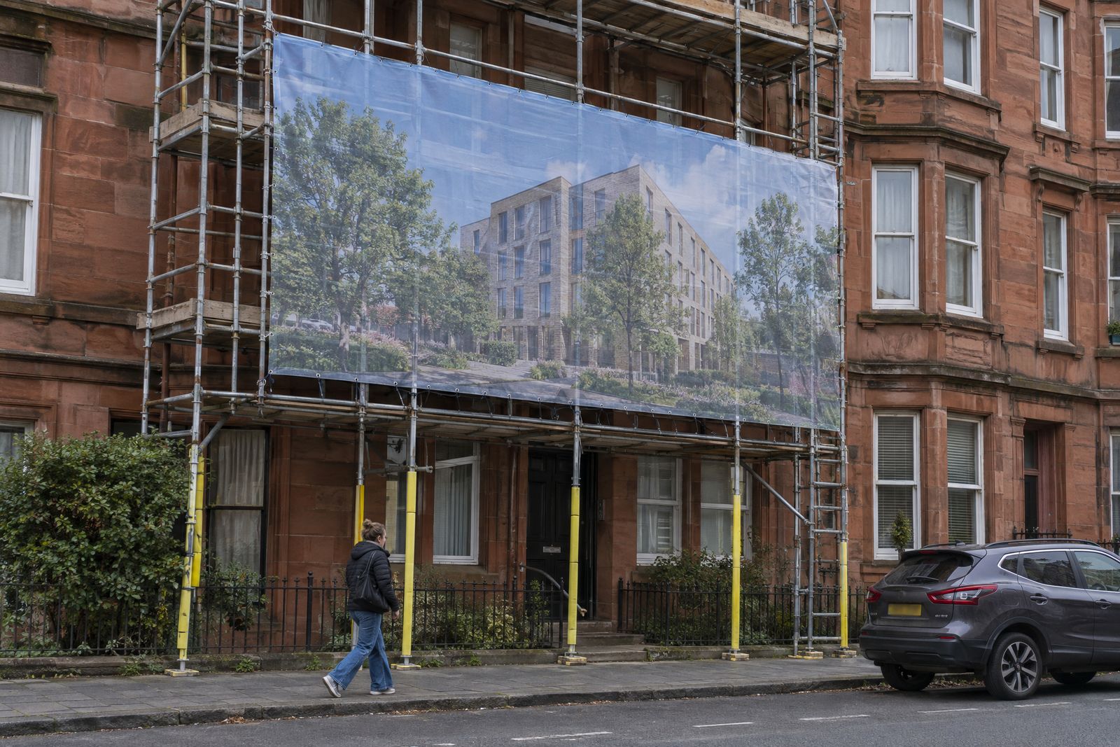 Printed mesh banner tied to scaffolding on a sandstone tenement