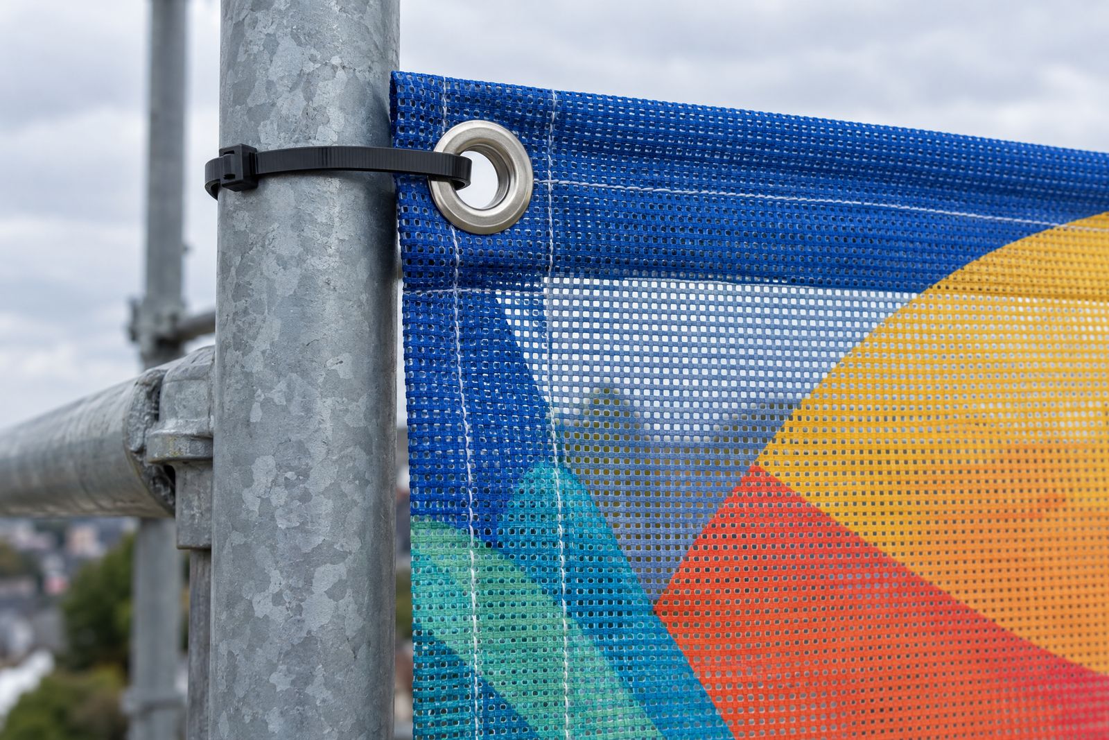 Mesh banner hem and eyelet cable-tied to a scaffold pole