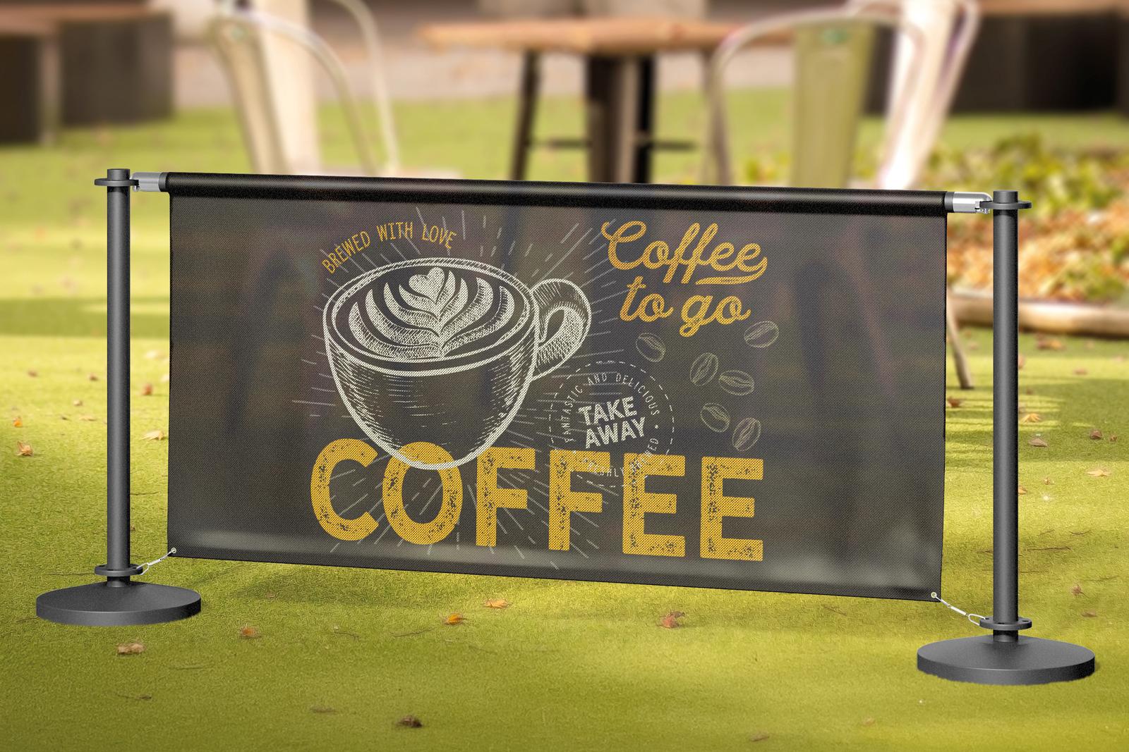 Black café barrier with a “Coffee to go” banner on a lawn outside a café