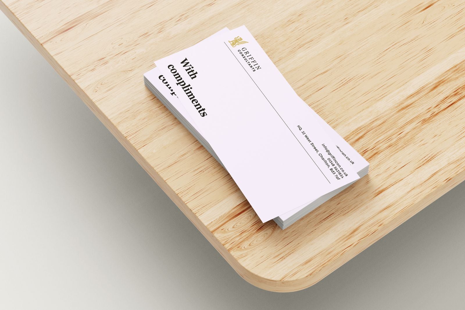 Stack of compliment slips with a griffin logo on a wooden desk
