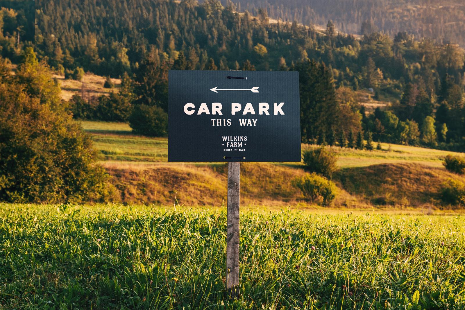 Black “Car park this way” correx sign on a post in a field