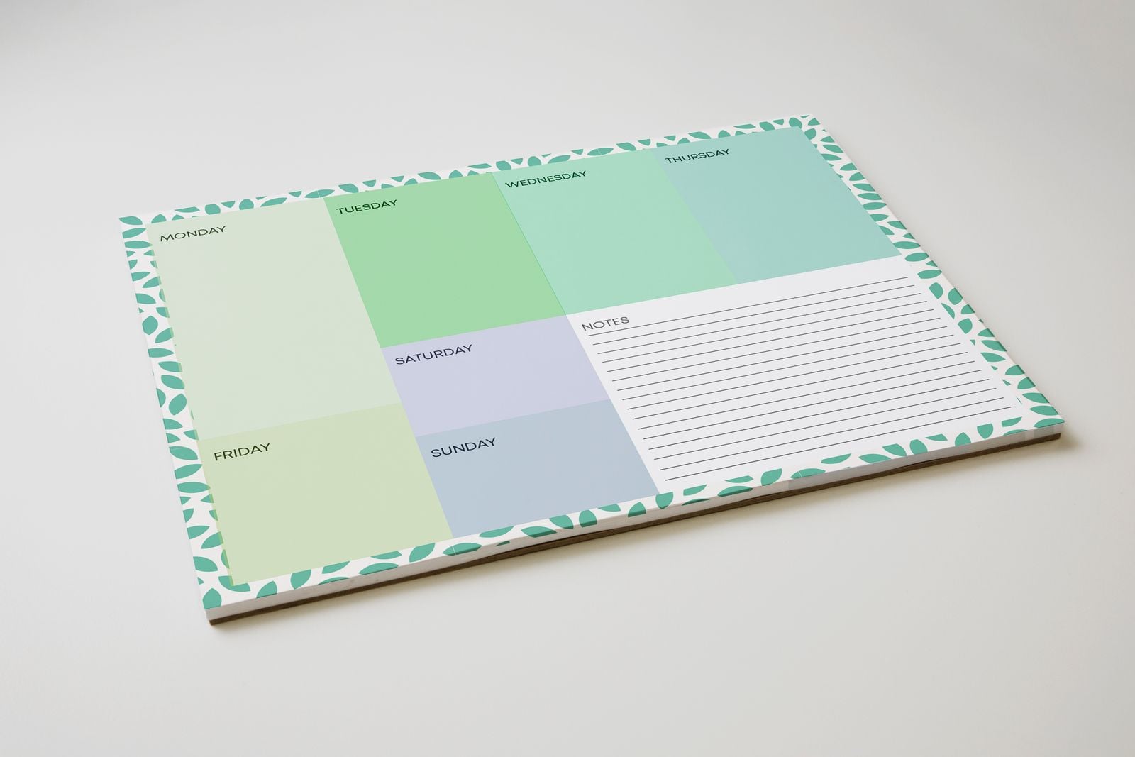 Weekly planner desk pad with green day boxes and a notes section