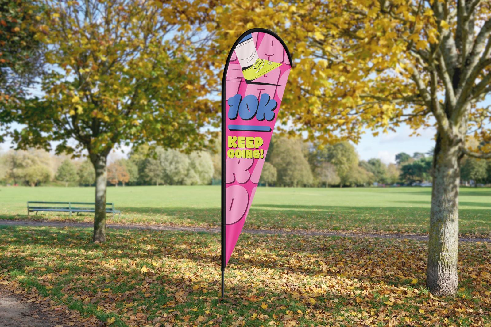 Pink “10k Keep going!” teardrop flag in a park in autumn