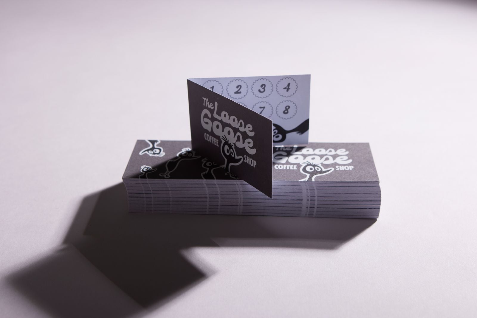 Grey coffee shop loyalty card standing open on a stack of folded cards, showing the stamp boxes inside