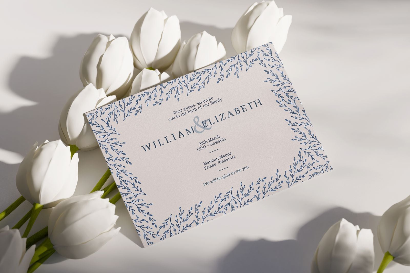 Wedding invitation with a blue leaf border, laid among white tulips