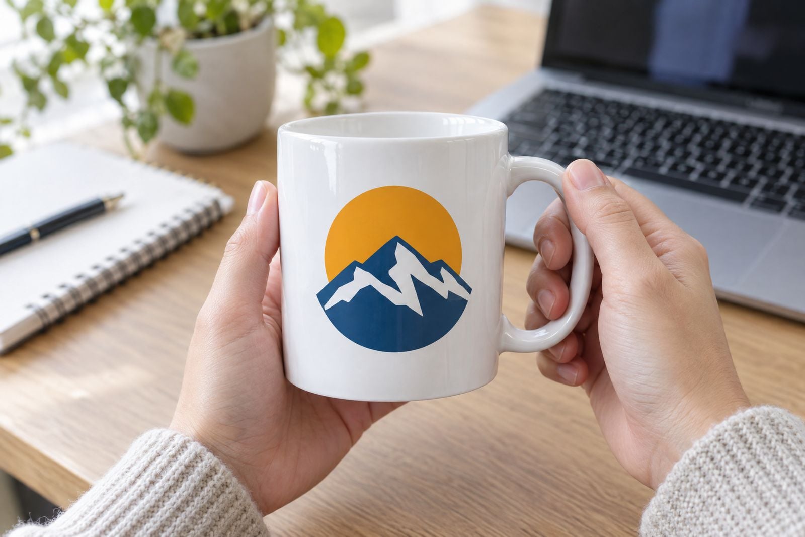 White mug printed with a mountain emblem, held at a desk