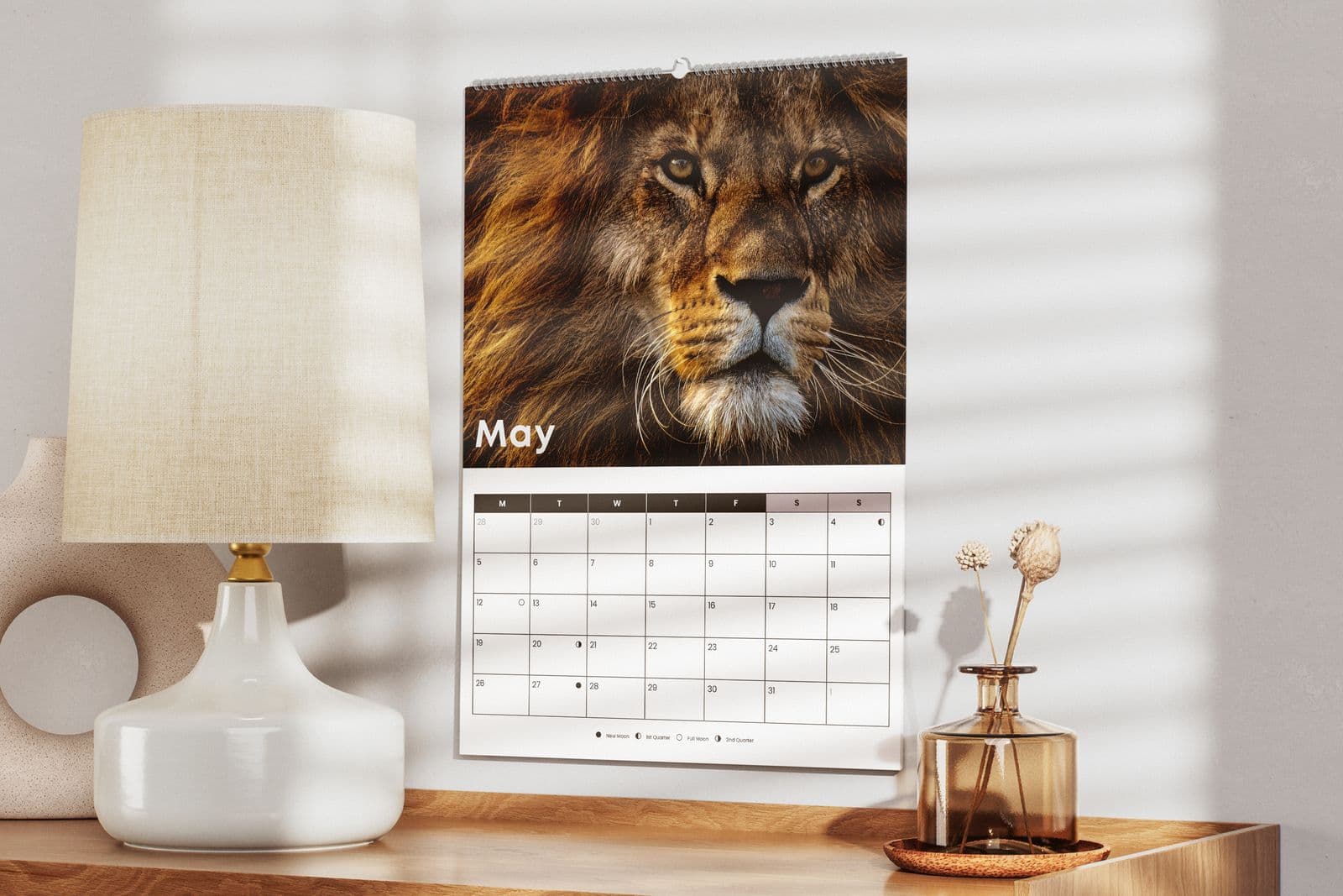 Wall calendar with a lion photo above a May grid, hanging over a sideboard